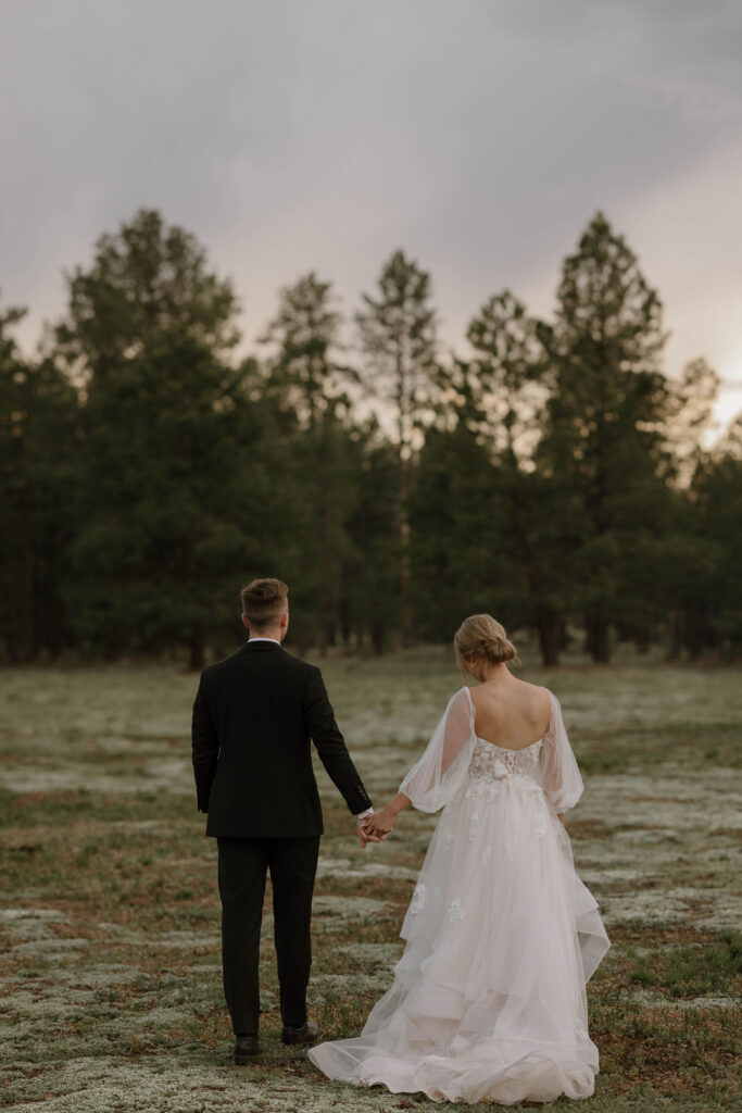 bride and groom walking together in the forest while holding hands