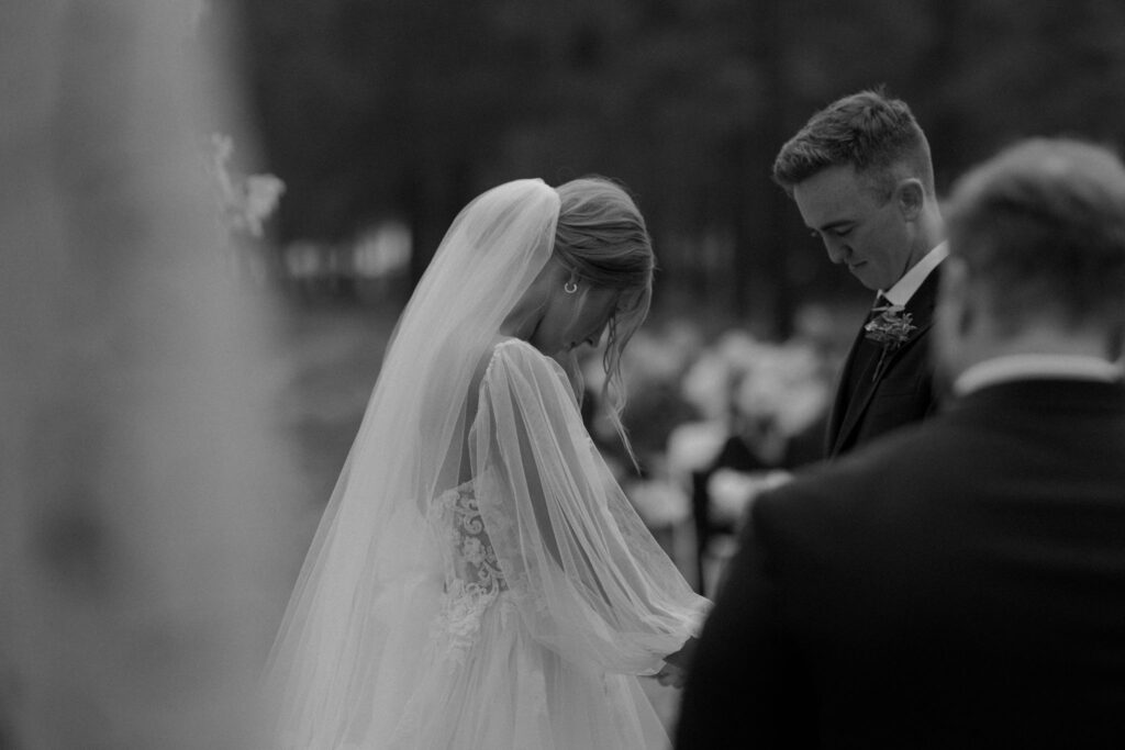 ceremony photo of groom holding hands at arbor with bride while they are praying during outdoor wedding day at arizona nordic village