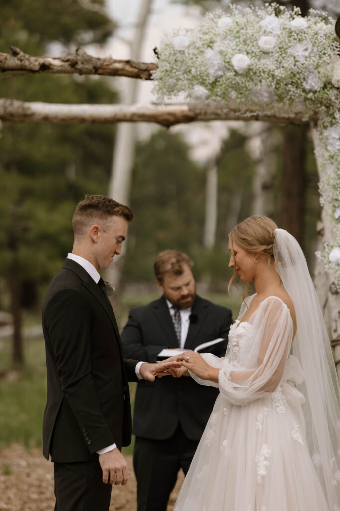 ceremony photo of groom holding hands at arbor with bride during outdoor wedding day at arizona nordic village