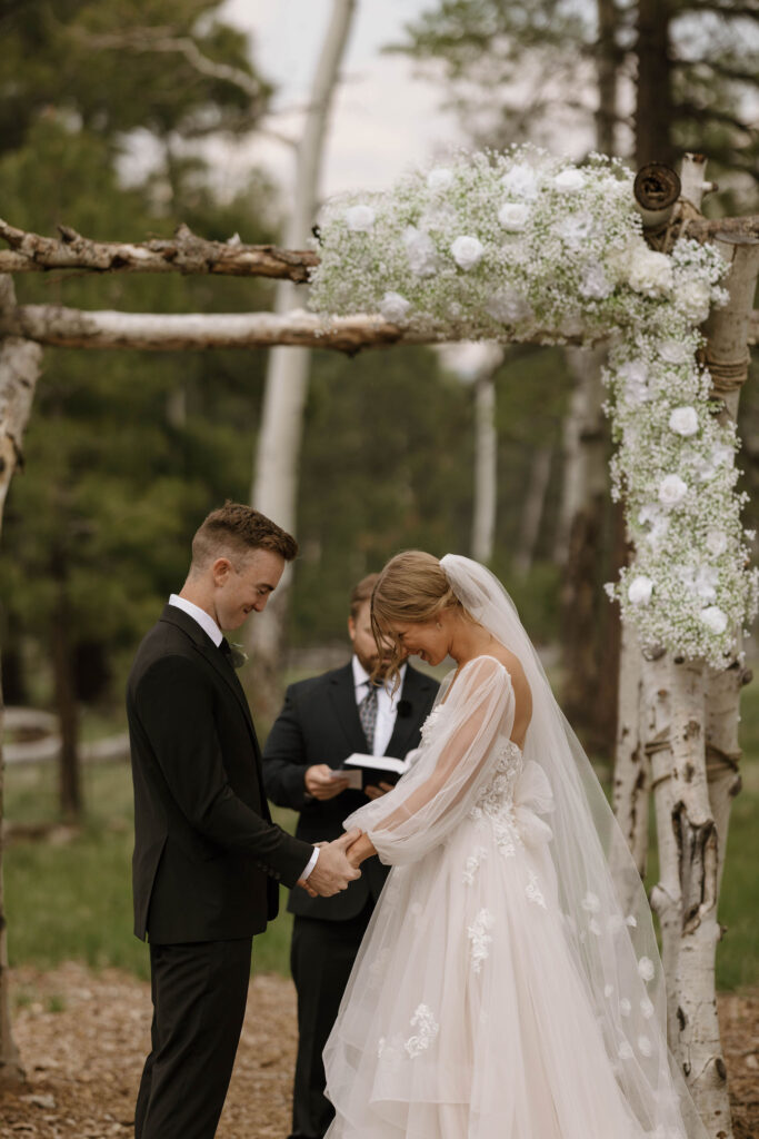 ceremony photo of groom holding hands at arbor with bride during outdoor wedding day at arizona nordic village